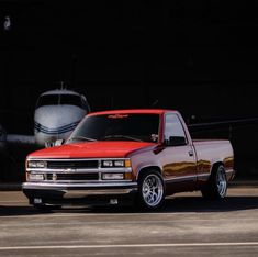 a red pick up truck parked next to an airplane