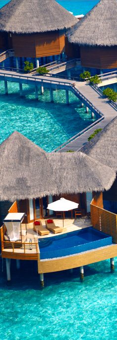 an over water resort with thatched roofs and lounge chairs on the deck, surrounded by clear blue water