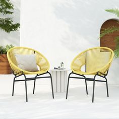 two yellow chairs sitting next to each other near a white table and potted plant