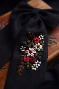 a black neck tie with flowers and pine cones on the side, sitting on a wooden surface