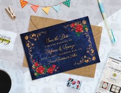 a blue wedding card with red flowers on it next to a cup of coffee and other items