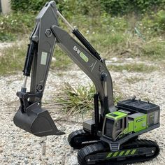 a green and black toy excavator sitting on top of a gravel field