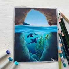 some colored pencils are next to an art work with dolphins in the water and underwater scene