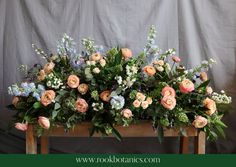 a wooden table topped with lots of flowers and greenery next to a gray wall