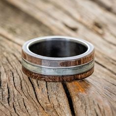 a wooden ring with silver inlays sits on a piece of wood