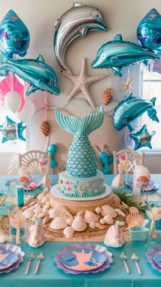 a table topped with lots of blue and pink balloons next to a starfish cake