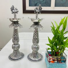 two silver candlesticks sitting on top of a table next to a potted plant