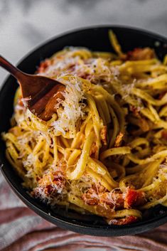 a pan filled with spaghetti and sauce on top of a tablecloth next to a wooden spoon