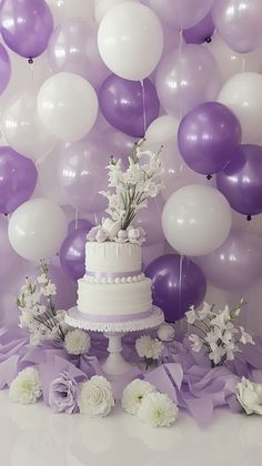 a wedding cake surrounded by balloons and flowers on a table in front of a purple backdrop