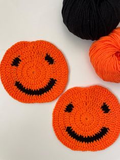 two crocheted pumpkin coasters with black and orange yarn on the top one has a smiling face