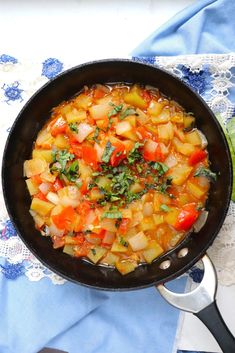 a skillet filled with vegetables on top of a blue and white table cloth next to silver spoons