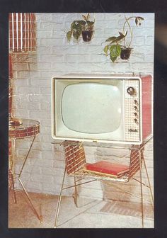 an old tv sitting on top of a table next to a chair and potted plants