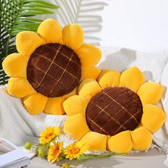 two yellow sunflower cushions sitting on top of a white blanket next to a plant