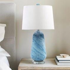 a blue vase sitting on top of a night stand next to a white pillow and lamp