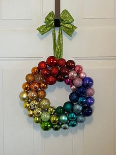 a wreath made out of christmas ornaments hanging on a door with a green bow around it