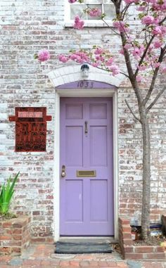 a purple door in front of a white brick building with pink flowers on the tree