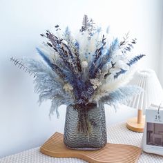 a vase filled with blue and white flowers on top of a wooden table next to a lamp