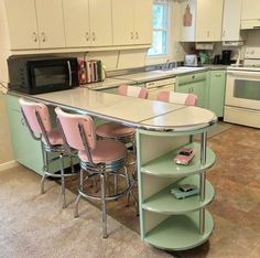 a kitchen with green cabinets and pink chairs in the center, an island that has four stools on it