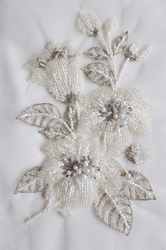 some white flowers and leaves are on a bed sheet or tablecloth with beading