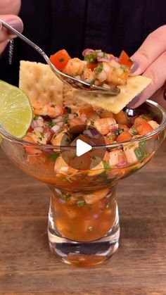 a person holding a spoon over a glass bowl filled with salsa and tortilla chips