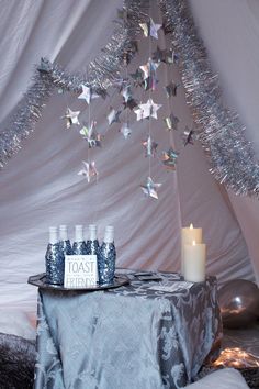 a table topped with bottles and a candle next to a white wall covered in tinsel