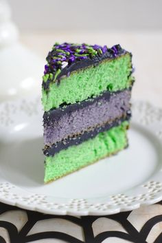 a slice of cake on a white plate with purple, green and black frosting