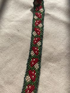 a green, red and white beaded bracelet on top of a white cloth covered table