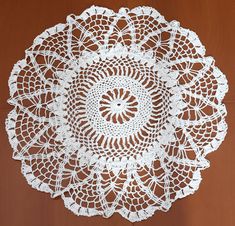 a crocheted doily is shown on a brown surface with white flowers and leaves