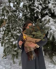 a woman standing in the snow holding a christmas tree