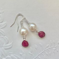 Sterling silver Pearl and Ruby earrings featuring sterling silver bezel set genuine faceted Rubies and beautiful high lustre white nucleated Pearls. I have finished the earrings with 925 sterling silver shepherd hooks and findings. A stunning pair of earrings that will make a perfect gift for June or July babies as Ruby is July's birthstone and Pearls are one of June's birthstones. * The Ruby bezels measures approximately 12mm x 8mm. * The nucleated pearls measure approximately 9mm x 9mm. * The Handmade Briolette Pearl Earrings For Gift, White Pearl Earrings In Sterling Silver, Elegant Silver Earrings For Birthday, Briolette Pearl Earrings With Gemstone For Gift, Gemstone Dangle Pearl Earrings For Anniversary, Dangle Pearl Earrings With Gemstone For Anniversary, Mother's Day Pearl Drop Dangle Jewelry, White Gemstone Drop Earrings, Mother's Day Dangle Pearl Drop Jewelry