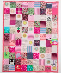 a patchwork quilt is hanging on the wall in front of a white wall with pink and green accents