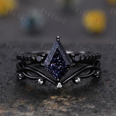 a black diamond ring with blue and white diamonds on it's sides, sitting on top of a stone surface