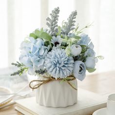 a white vase filled with blue flowers sitting on top of a table next to a cup and saucer