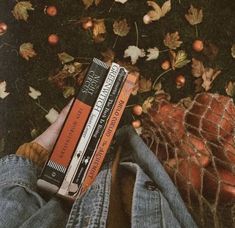 a person is holding three books in their hands while laying on the ground with autumn leaves