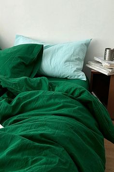 an unmade bed with green sheets and pillows on top of it, next to a night stand