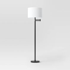 a black floor lamp with a white shade on the top, and a metal base