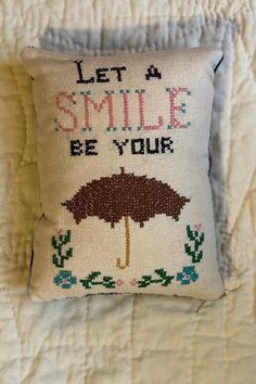 a cross stitch pillow with an umbrella on it that says, let a smile be your