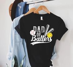 a t - shirt that says dad of ballers hanging on a rack with clothes