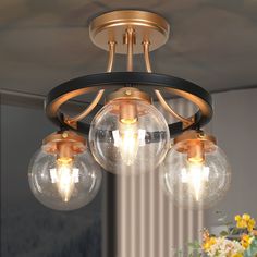 three clear globes are hanging from a chandelier in a room with flowers