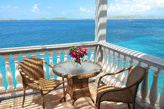 two chairs and a table on a balcony overlooking the ocean with flowers in a vase