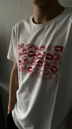 a man standing in front of a wall wearing a white shirt with red letters on it