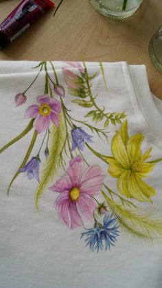 a white t - shirt with colorful flowers painted on the front and back, sitting on a wooden table