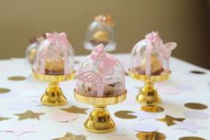 three small cakes in glass domes on top of a table covered with confetti