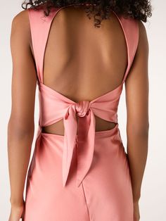 the back of a woman wearing a pink dress with cutouts and a bow tie