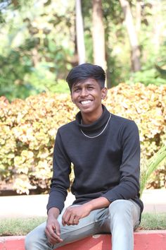 a young man sitting on top of a red brick wall next to bushes and trees