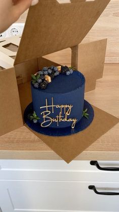 a blue birthday cake sitting on top of a wooden table next to a cardboard box