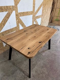 a wooden table sitting on top of a cement floor next to a wall covered in plywood