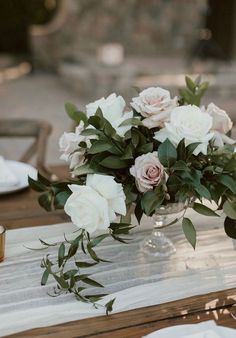 a vase filled with white flowers sitting on top of a wooden table next to plates