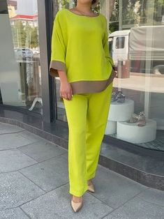 a woman standing in front of a store window wearing bright green pants and a yellow top