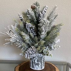 a white vase filled with lots of snow and pine cones on top of a wooden table